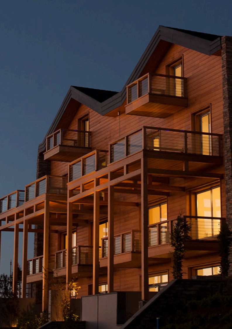 Le chalet privé de Tilal Faqra livré, façades bois et balcons éclairés au crépuscule.